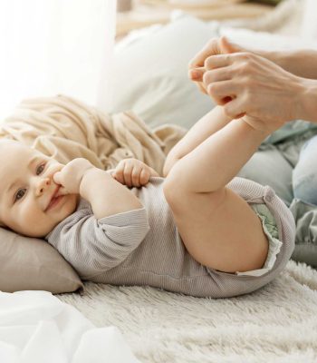 cierrese-encima-retrato-pequeno-hijo-recien-nacido-que-miente-cama-mientras-que-juega-madre-kid-sonriendo-metiendo-dedos-boca-luciendo-feliz-despreocupado